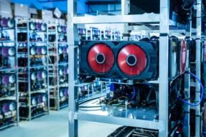 Rows of metallic shelves hold powerful computers with red circular fans in a large, brightly lit cryptocurrency mining facility.